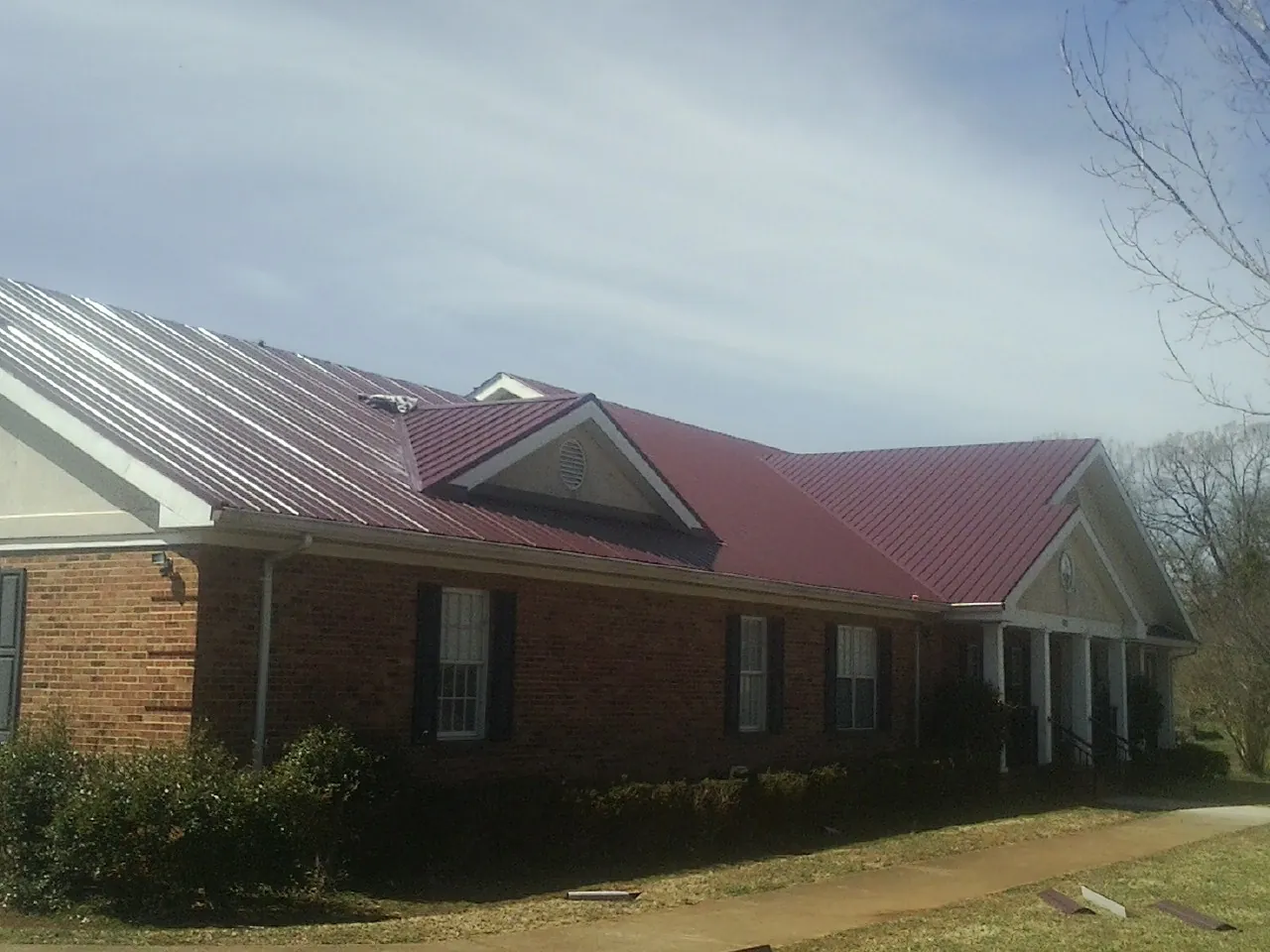Red metal roof with gabled entries on a long brick building, from a Hail Damage Roof Repair job in Oregonia