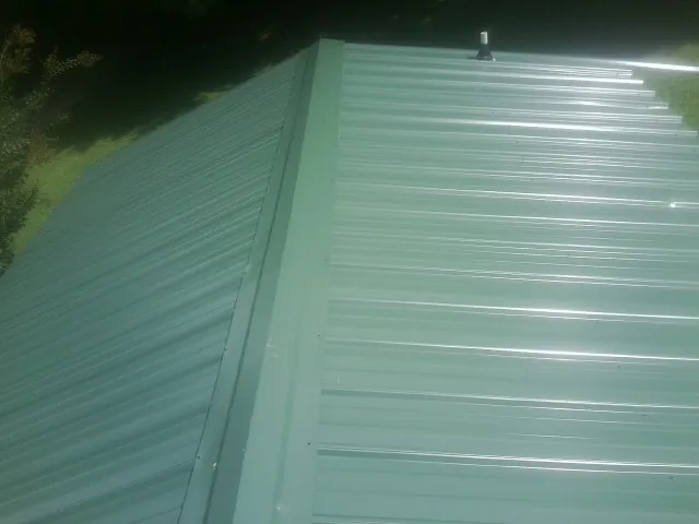 New green metal panels meeting at the ridge of a roof — Flat Roof Repair work by our crew in Oregonia