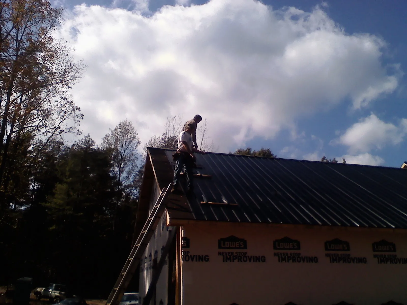 Roofer fastening dark metal panels high against a cloudy sky, from a Roof Inspection job in Oregonia