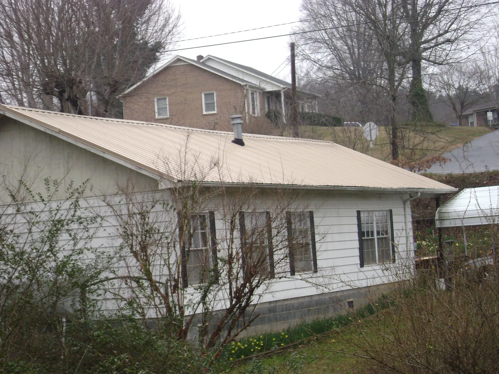 Tan metal roof on a white sided house set into a hillside — Commercial Roofing by Roofing Brothers in Oregonia